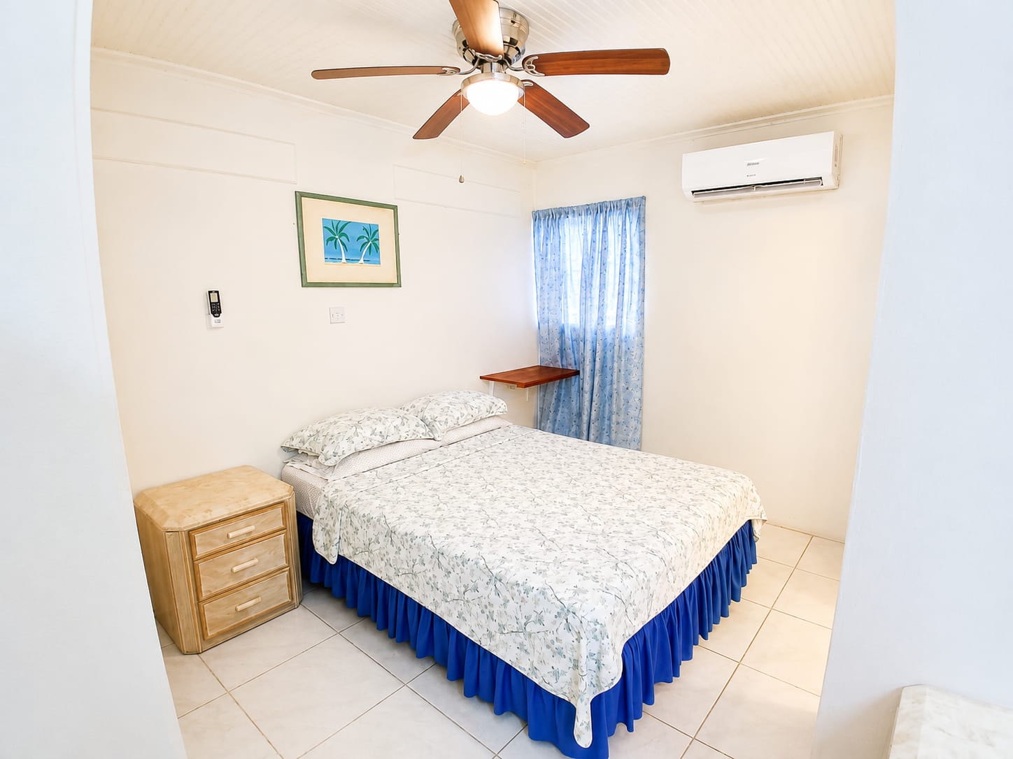 Cozy bedroom with floral bedspread, blue curtains, and ceiling fan